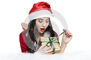 Excited young woman opening a Christmas gift. Cute girl in a Santa Claus costume unleashes a ribbon on a new year gift lying on