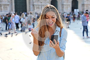 Excited young woman receiving good news on line in a smart phone