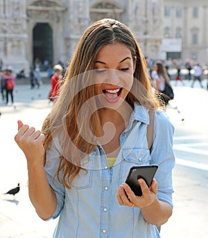 Excited young woman receiving good news on line in a smart phone