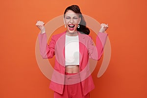 Excited young woman standing isolated over orange background make winner gesture
