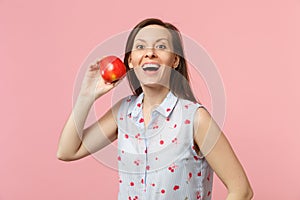 Excited young woman in summer clothes holding fresh ripe red apple fruit isolated on pink pastel wall background, studio