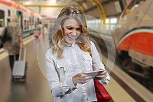 Excited young woman using smartphone on blurred metro subway station background.