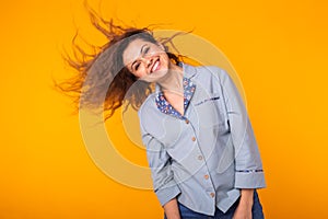 Excited young woman waving hair in blue home wear, widely smiling having fun. Isolated on yellow background.