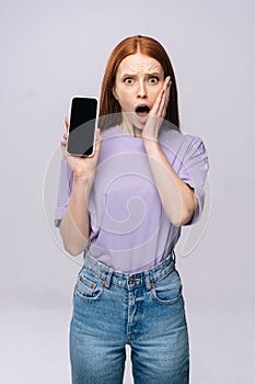 Excited young woman wearing stylish casual clothes holding cell phone with black empty mobile screen