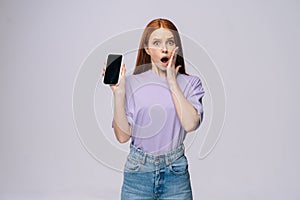 Excited young woman wearing stylish casual clothes holding cell phone with black empty mobile screen