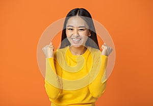 excited young woman in a yellow sweater clenches fists have good mood feel happy excited emotion on orange background