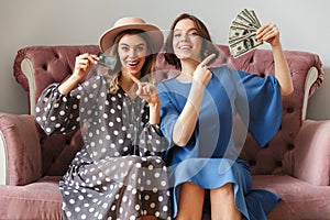 Excited young women shopaholics holding money and credit card.