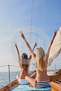 Excited young women with their arms raised cheering making peace signs on cruise. Happy friends on holiday making peace