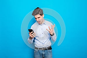 An excitedly shouting man is talking on a smartphone and shouting into the phone, standing on blue background