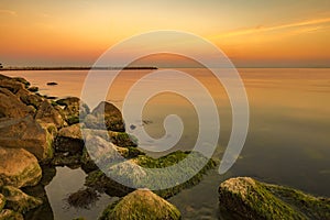 Exciting sea sunset at warm colors and colorful moss over the rocks.