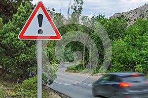 An exclamation mark on a road sign warning of danger and a fast-moving car