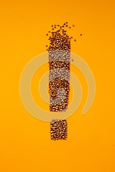 Exclamation point shape of buckwheat groat on orange background