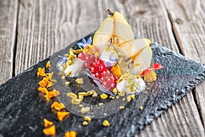 Exclusive autumn cream dessert with pears, currants and pistachios on black board, decorated with flowers petals, product