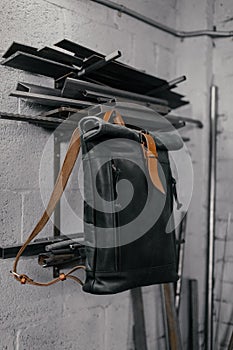 Exclusive black leather backpack. Backpack near the wall. The tools in the garage. Metal pipes near the wall