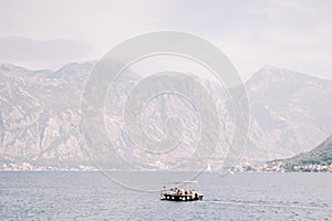 Excursion boat sails on the sea against the backdrop of a mountain range in a light haze