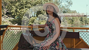 Excursions by river tram. A beautiful young woman in a straw hat and dress is sitting and admiring nature. The concept