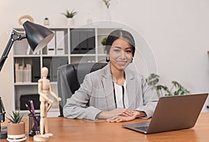 Executive Asian businesswoman sitting on desk in office