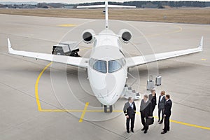 Executive business team in front of corporate jet talking to pil