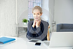 Executive businesswoman looking at camera and smiling while sitting at office desk and working