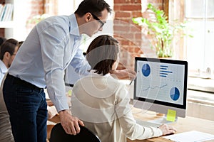 Executive manager helping employee preparing online statistical report in office photo