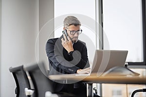 Executive middle aged businessman having a call and using laptop while working at the office