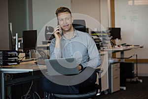 Executive talking on mobile phone while using laptop