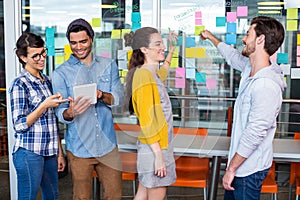 Executives discussing over sticky note on glass wall