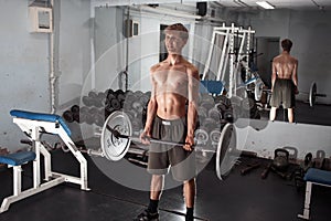 Exercise on the biceps with the barbell. A young lean athletic man performs.
