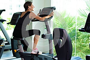 Exercise bike cardio workout at fitness gym of woman taking weight loss. female listens to music on headphones. Athlete