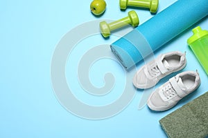 Exercise mat, dumbbells, apple, towel, shaker and shoes on light blue background. Space for text