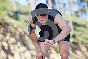 Exercise, watch and time with a sports man tracking his fitness on a sport app while running outdoor in nature. Training