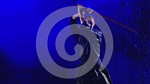 Exercise with a wooden sword of a kendo master in a blue kimono under streams of rain. Shot in slow motion on a smoky