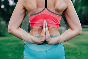 Exercises for proper posture. Body of young woman in pink top and blue sports trousers with her palms folded behind her