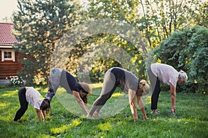 Exercising females of four generations of family warming up with hands on ground stretching their bodies on meadow full