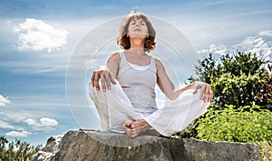 Exercising outside for radiant 50s yoga woman sitting on ston