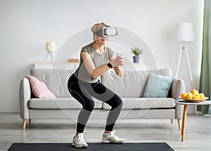 Exercising with virtual reality concept. Athletic mature woman in VR headset doing squats on her home workout