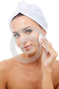 Exfoliation is the key to great skin. Beautiful young woman applying toner on to her face while isolated against a white