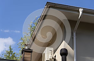 Exhaust air pipes, air conditioner and white rain gutter on private house roof. Metallic Guttering System and