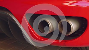 Exhaust gas goes out from twinned exhaust pipe of red sport car