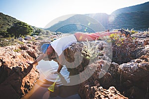 Exhausted adventurer drinks water from a crevice in a rock