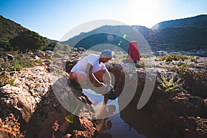 Exhausted adventurer drinks water from a crevice in a rock