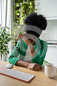 Exhausted African American woman having headache sits at office desk with keyboard. Burnout.