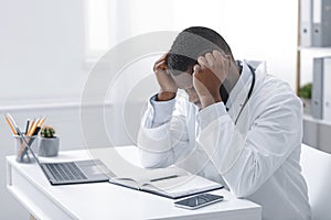 Exhausted african doctor sitting in office in front of laptop