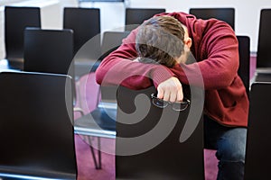 Exhausted boy holding glasses and sleeping in meeting room