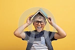 Exhausted boy schooler with book on his head, yellow background