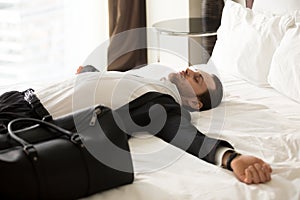 Exhausted businessman laying on bed in hotel room.