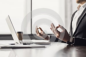 Exhausted businessman meditating in office. Tired men relaxing and doing yoga during work. Male hands in mudra close up view.