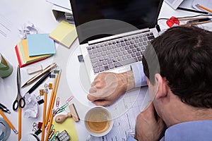 Exhausted Businessman Resting On Messy Desk With Open Laptop