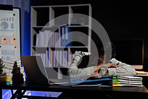 Exhausted businessman sleeping at his desk and working overtime late at night, he is surrounded by piles of paperwork