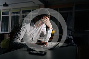 Exhausted businessman working in evening office alone. Tired anxious manager losing failure working on computer at late